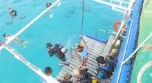Divers preparing to enter the water from a boat in Phuket, Thailand, with clear blue water.
