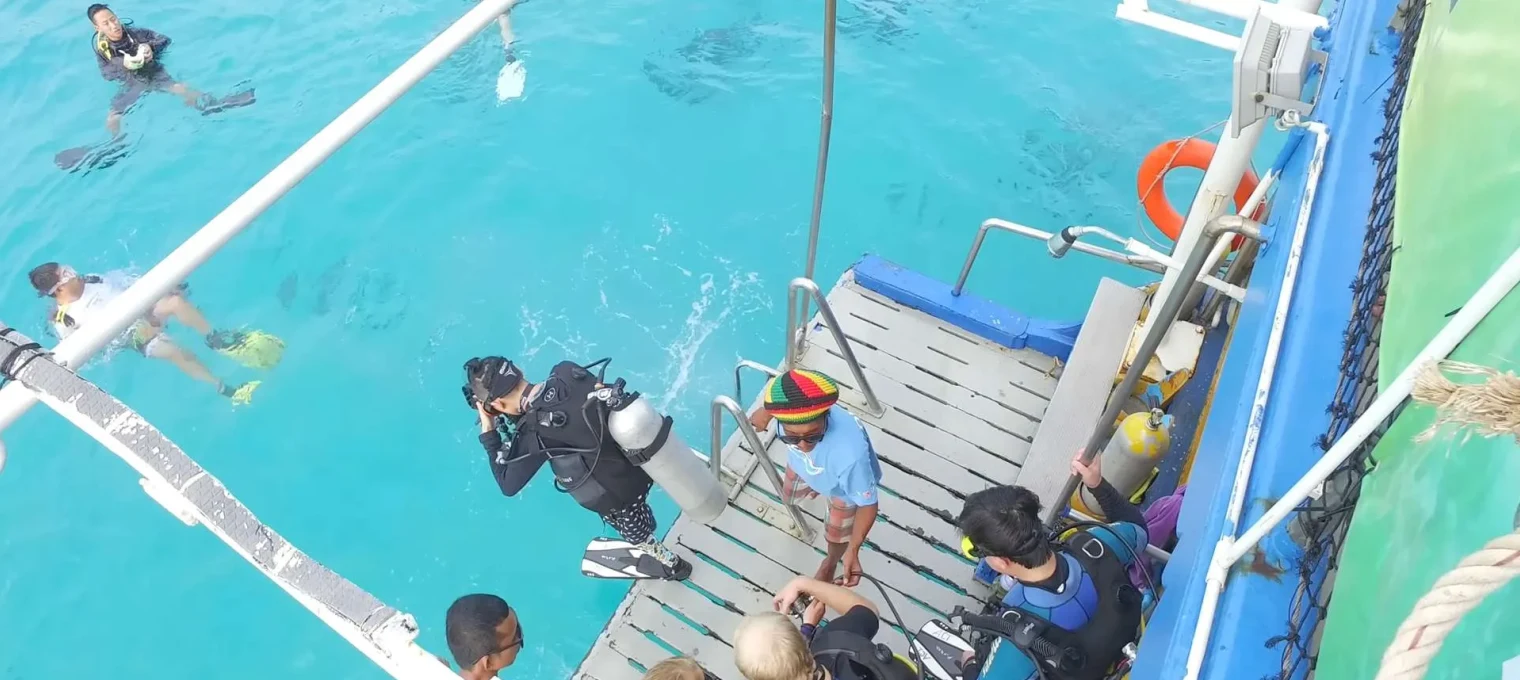 Divers preparing to enter the water from a boat in Phuket, Thailand, with clear blue water.