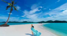 Woman in a blue striped dress walking on a white sandy beach in Phuket, Thailand.