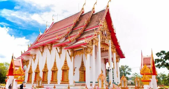 Храм в Пхукете с красной крышей и золотыми деталями, на фоне голубого неба.