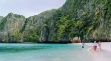 Two people walking in shallow water on a picturesque beach surrounded by cliffs in Phuket.