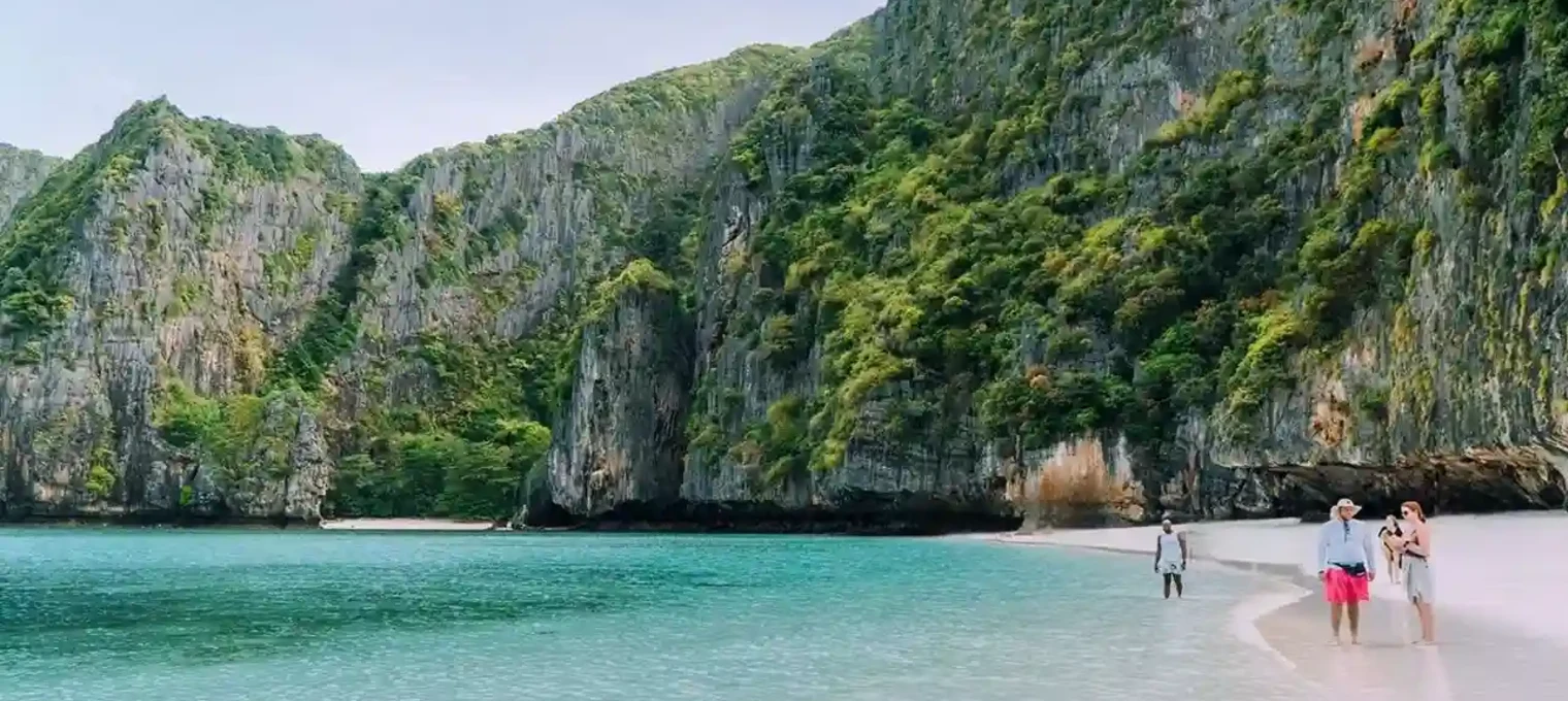 Two people walking in shallow water on a picturesque beach surrounded by cliffs in Phuket.