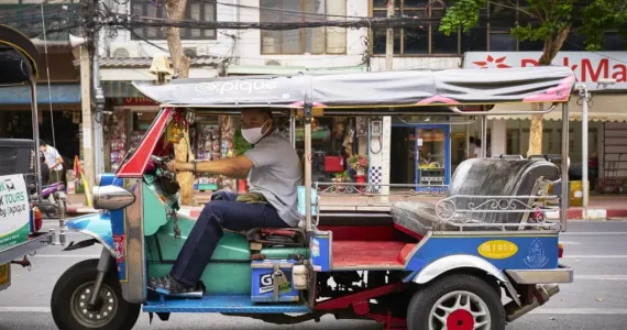 A tuk-tuk driver operating in Phuket, surrounded by local shops and greenery.