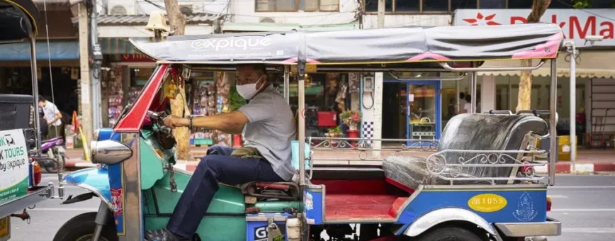 A tuk-tuk driver operating in Phuket, surrounded by local shops and greenery.