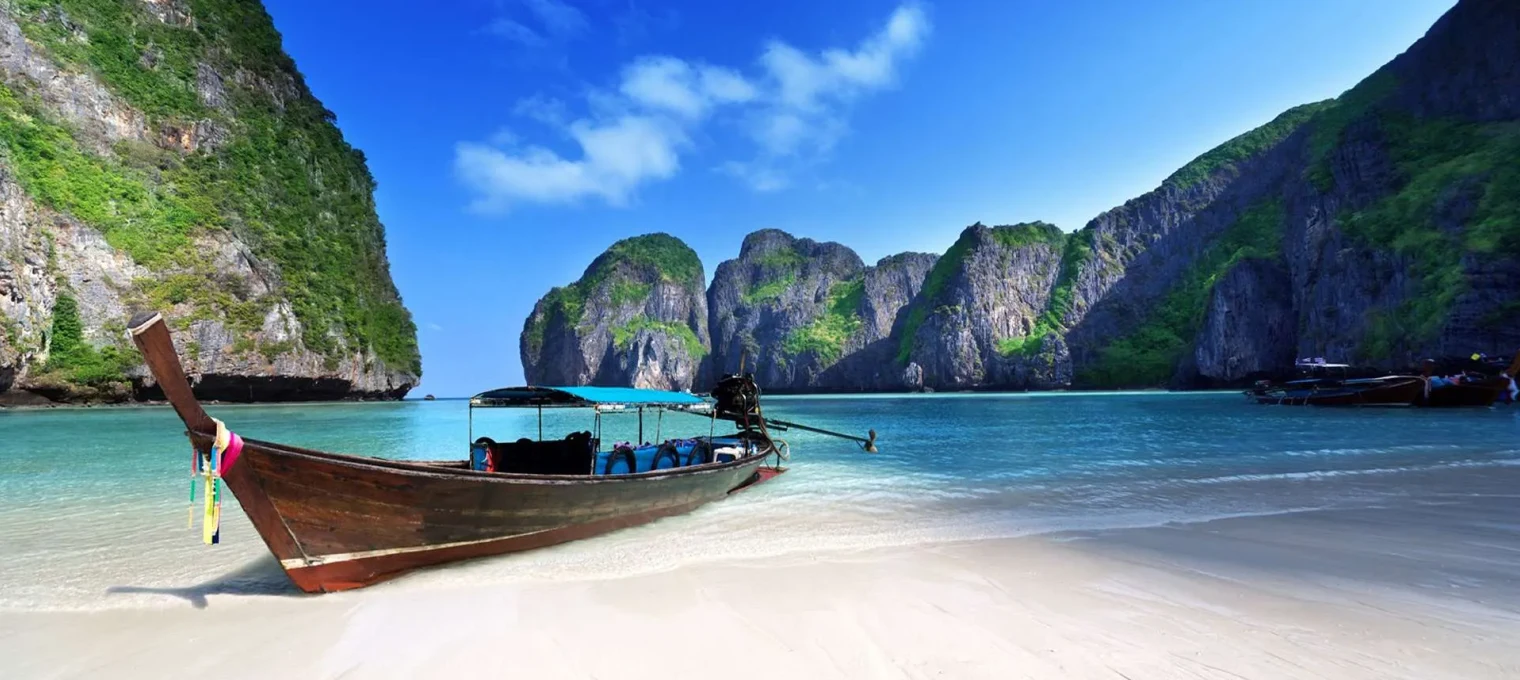 Scenic view of a traditional boat on a serene beach in Phuket, surrounded by cliffs.