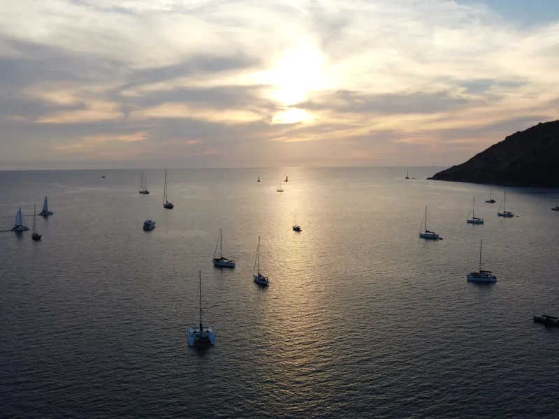 Sunset over Phuket, Thailand, with sailboats anchored in calm water.
