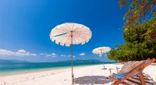 Beautiful beach scene in Phuket with white sand, umbrellas, and clear blue skies.