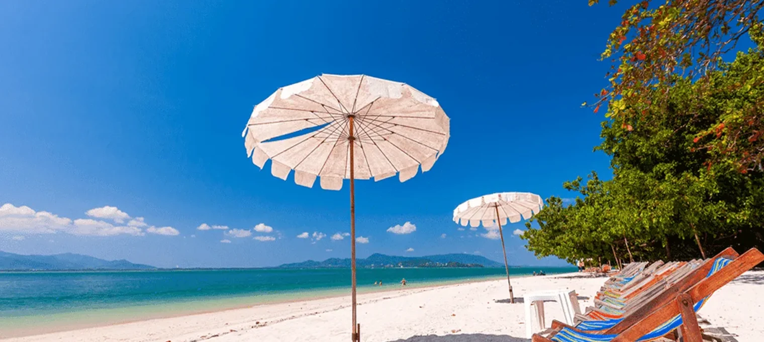 Beautiful beach scene in Phuket with white sand, umbrellas, and clear blue skies.