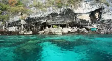 Scenic view of blue waters and rocky cliffs in Phuket, Thailand with a cave entrance.