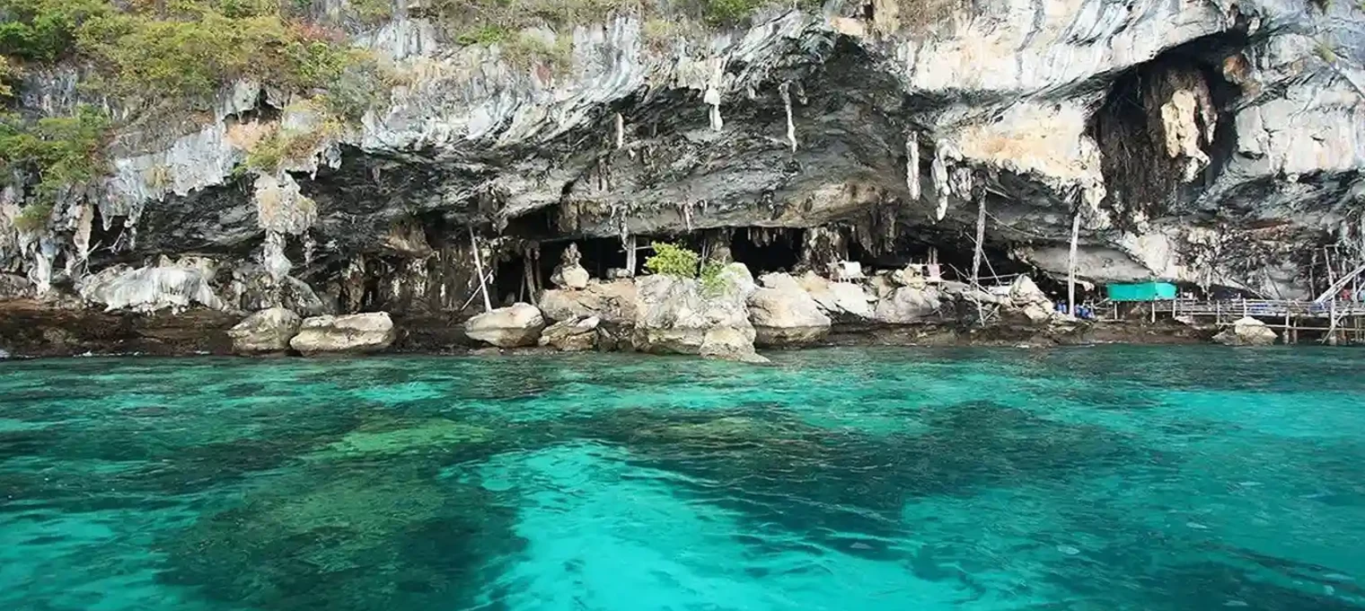 Scenic view of blue waters and rocky cliffs in Phuket, Thailand with a cave entrance.