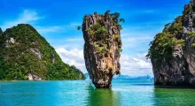 Tall limestone rock surrounded by turquoise water and lush green hills in Phuket, Thailand.