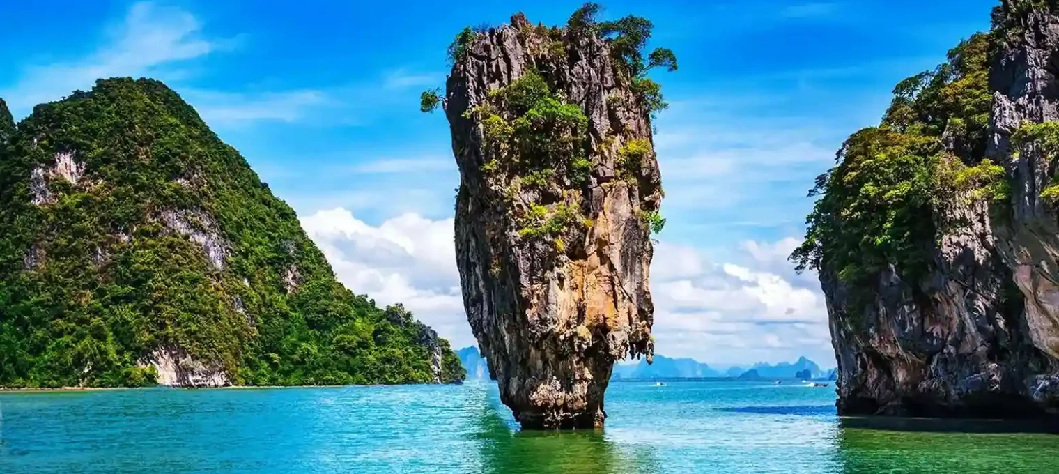 Tall limestone rock surrounded by turquoise water and lush green hills in Phuket, Thailand.