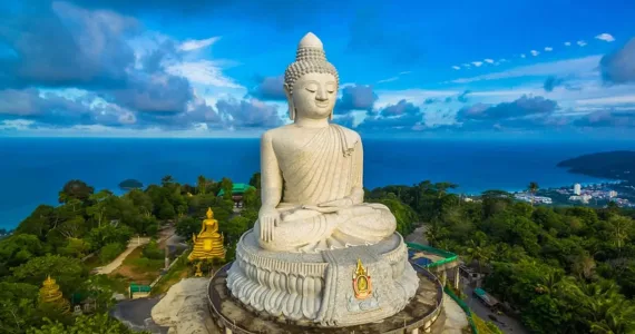 Majestic large Buddha statue overlooking the sea in Phuket, Thailand, surrounded by lush greenery.