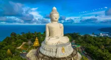 Majestic large Buddha statue overlooking the sea in Phuket, Thailand, surrounded by lush greenery.