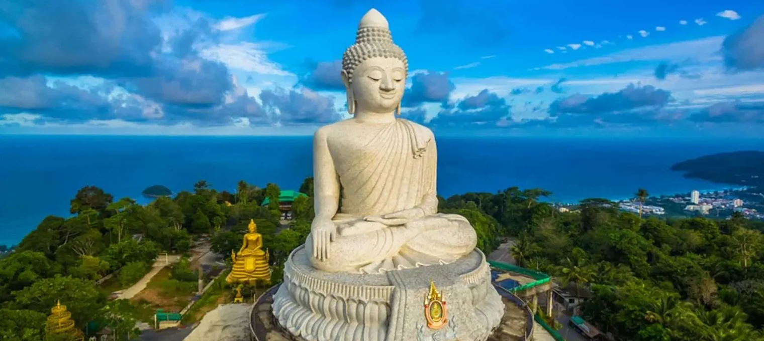 Majestic large Buddha statue overlooking the sea in Phuket, Thailand, surrounded by lush greenery.