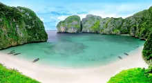Beautiful beach in Phuket with green cliffs and clear turquoise water. Boats on the shore.