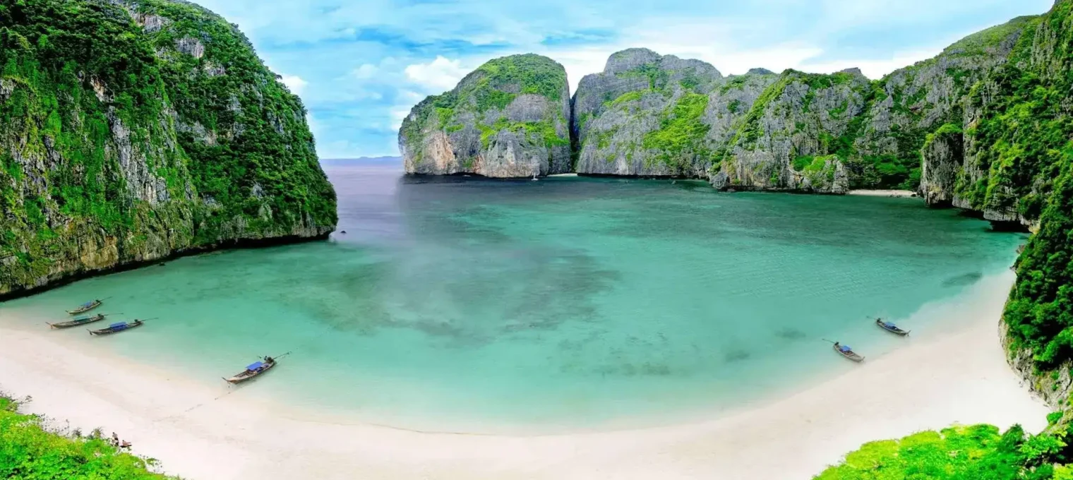Beautiful beach in Phuket with green cliffs and clear turquoise water. Boats on the shore.