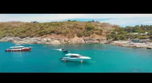 Boats anchored in clear turquoise waters near a rocky coastal area in Phuket.