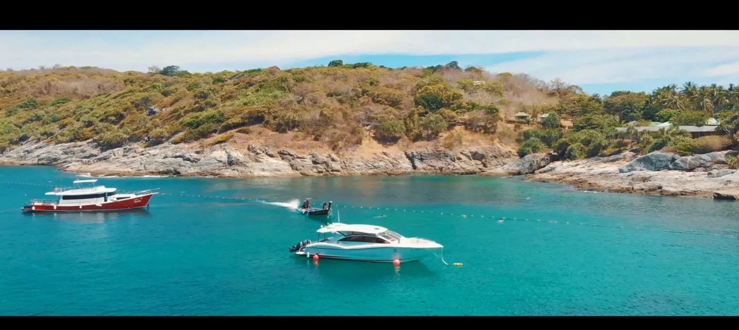Boats anchored in clear turquoise waters near a rocky coastal area in Phuket.