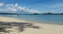 A serene beach in Phuket with clear blue waters and boats moored in the distance.