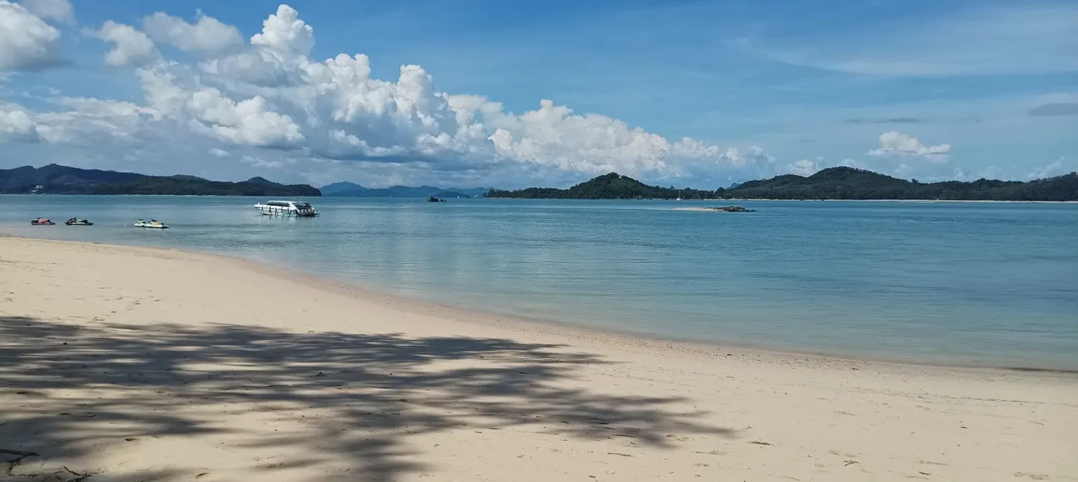A serene beach in Phuket with clear blue waters and boats moored in the distance.