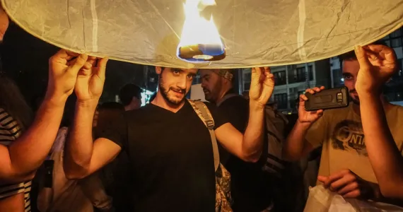 Мужчина с фонарем в руках на празднике в Пхукете, вокруг люди и огонь.