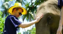 A young man in sunglasses and a straw hat gently pets an elephant in Phuket.