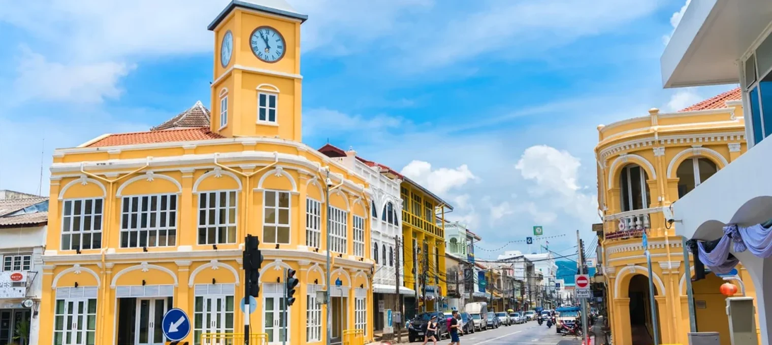 Желтые здания с часами на углу улицы в Пхукете под ясным небом.