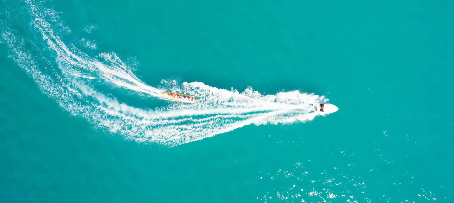 Aerial view of a jet ski and a colorful boat cutting through turquoise waters in Phuket.