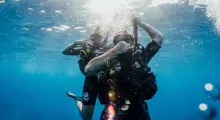 Two scuba divers giving a "shaka" sign underwater in Phuket, surrounded by blue water.