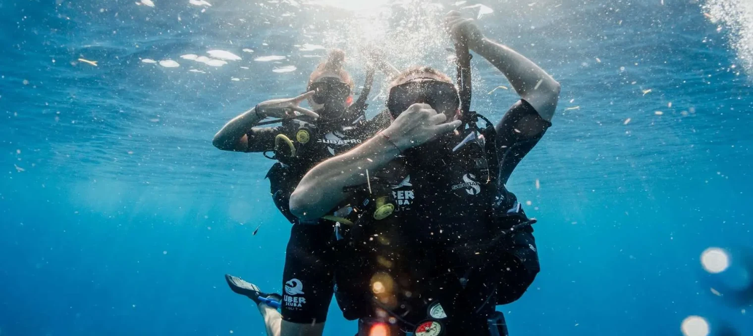 Two scuba divers giving a "shaka" sign underwater in Phuket, surrounded by blue water.