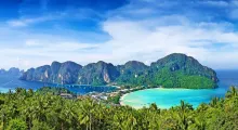 Stunning view of Phuket's coastline with lush greenery, clear blue waters, and mountains.