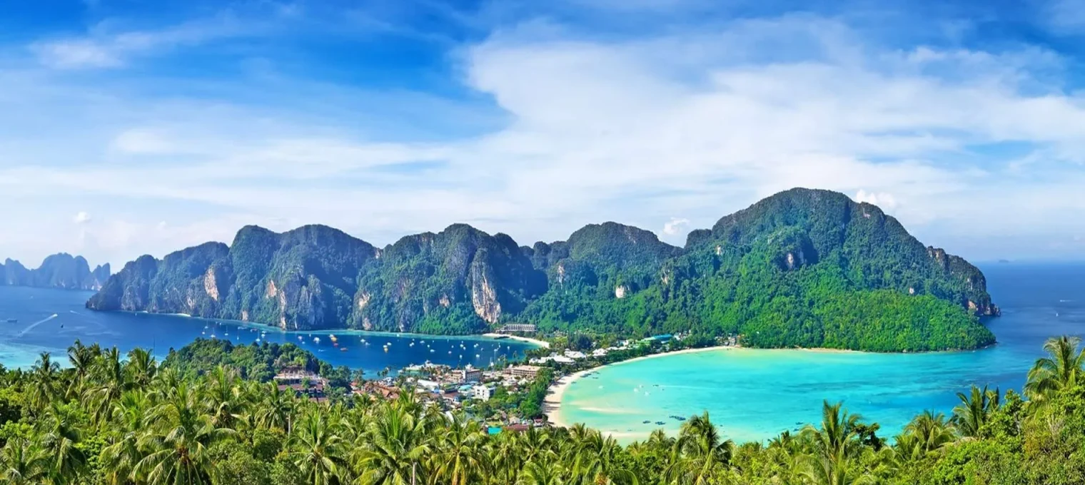 Stunning view of Phuket's coastline with lush greenery, clear blue waters, and mountains.