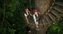 Two women in helmets enjoying a treetop adventure in Phuket, surrounded by lush greenery.