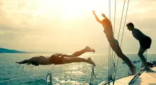 Two people diving into the water from a boat in Phuket at sunset.
