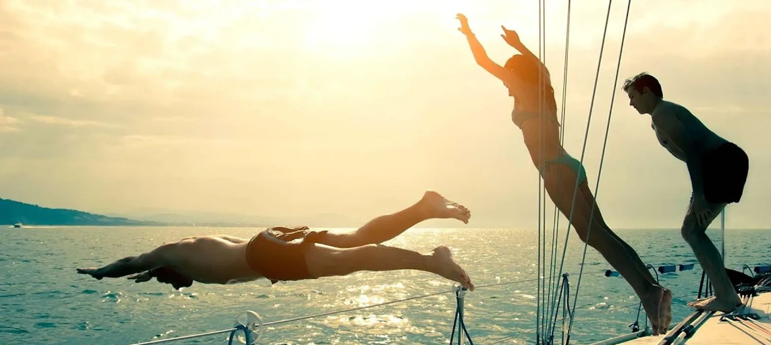 Two people diving into the water from a boat in Phuket at sunset.