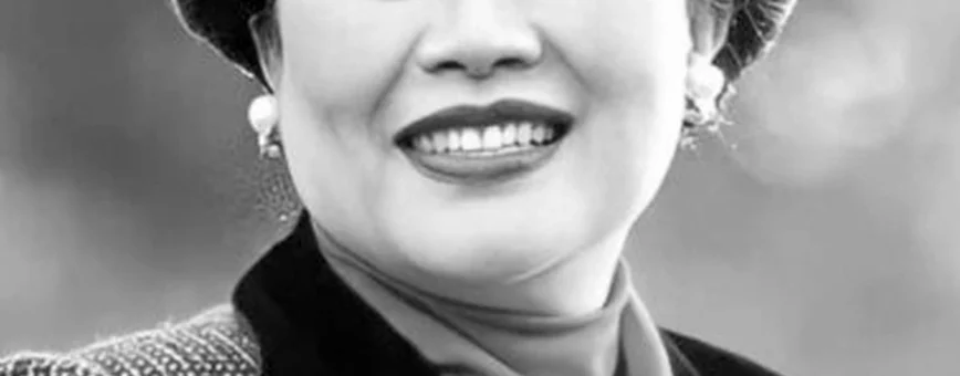 Женщина с улыбкой в элегантном наряде, позирующая на фоне природы.