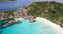 Aerial view of a secluded beach in Phuket with clear turquoise waters and rocky landscape.