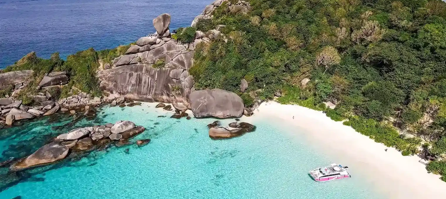 Aerial view of a secluded beach in Phuket with clear turquoise waters and rocky landscape.