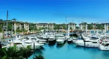 Luxury yachts docked at a marina in Phuket with palm trees and modern buildings nearby.