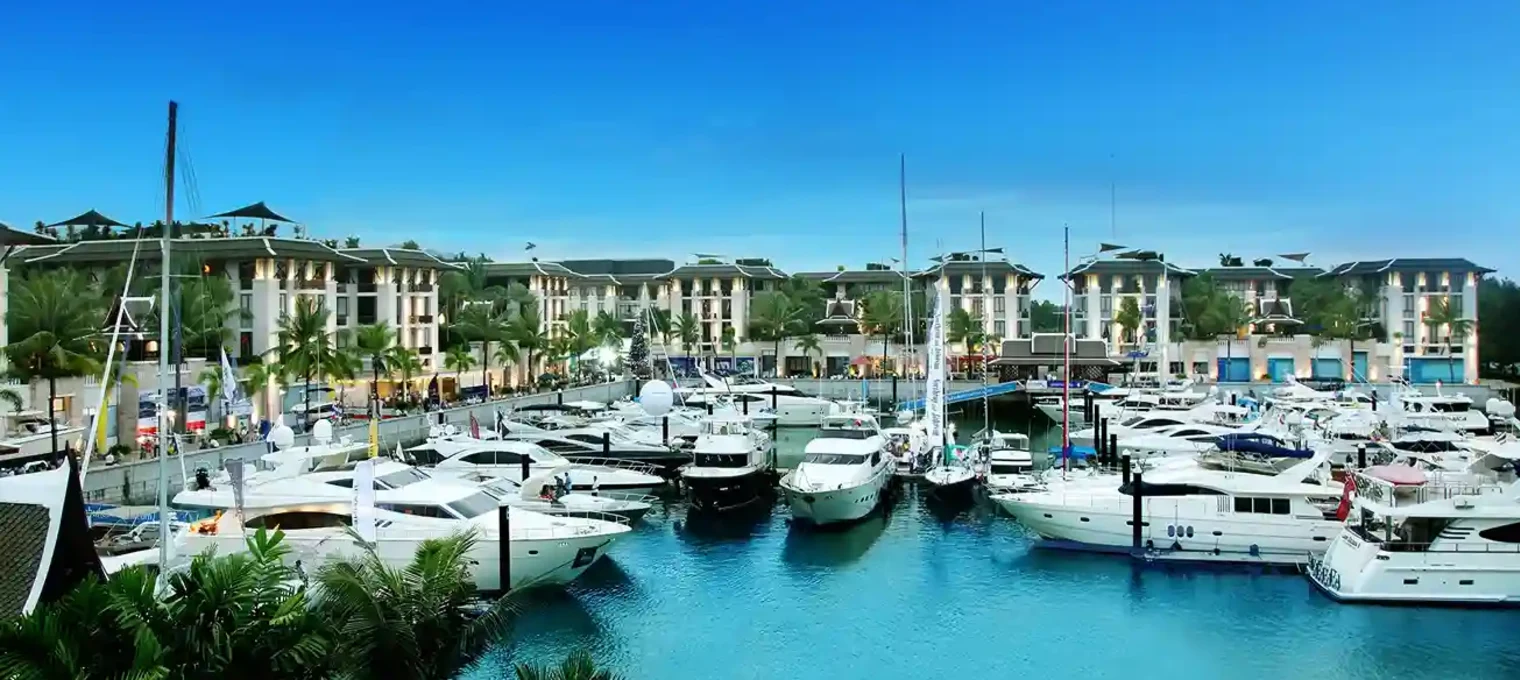 Luxury yachts docked at a marina in Phuket with palm trees and modern buildings nearby.