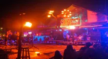 A fire performer leaps with flaming torches at a lively beach bar in Phuket.