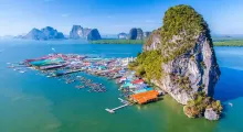 Colorful floating village near limestone cliffs in Phuket, Thailand, surrounded by clear water.