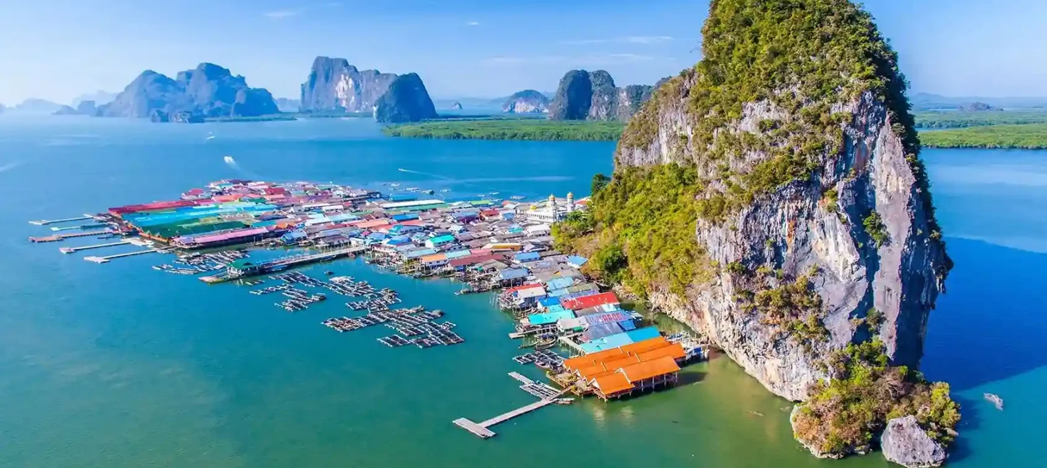 Colorful floating village near limestone cliffs in Phuket, Thailand, surrounded by clear water.
