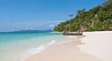 Serene beach in Phuket with clear waters, gentle waves, and fishing boats along the shore.