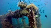 Underwater scene of a coral-covered shipwreck teeming with colorful fish in Phuket.