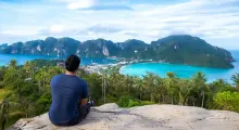 A person sitting on a rock overlooks the stunning coastline of Phuket with lush greenery.