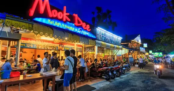 Ресторан Mook Dee в Пхукете, яркие огни и люди, наслаждающиеся ужином на улице.