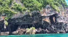 Lush rocky cliffs and cave formations near turquoise waters in Phuket, Thailand.