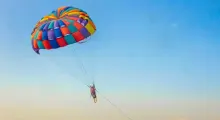 Person paragliding with a colorful parachute over a clear blue sky in Phuket.